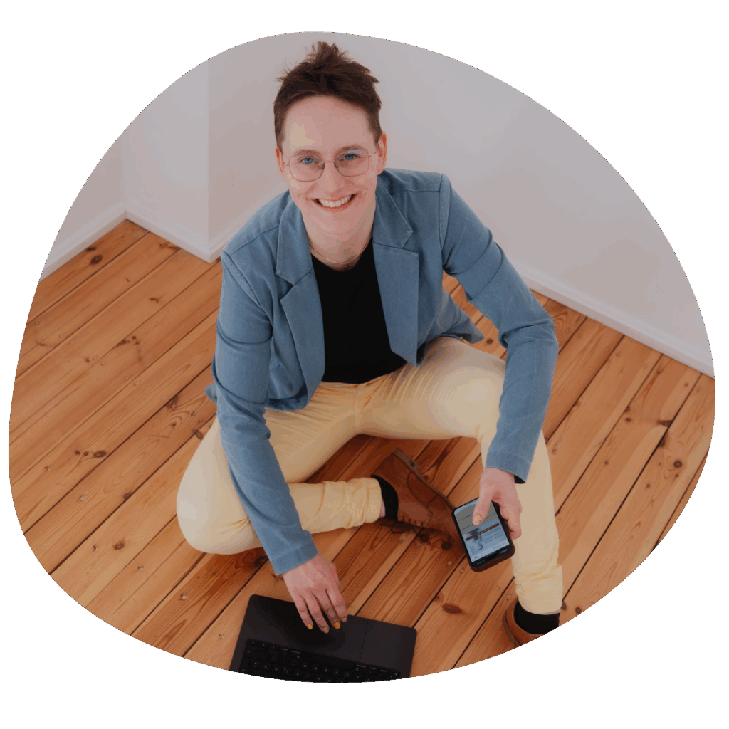 Antonia Ludwig, Psychologin und Job-Crafting-Expertin, sitzt lächelnd mit Laptop und Smartphone auf einem Holzboden.