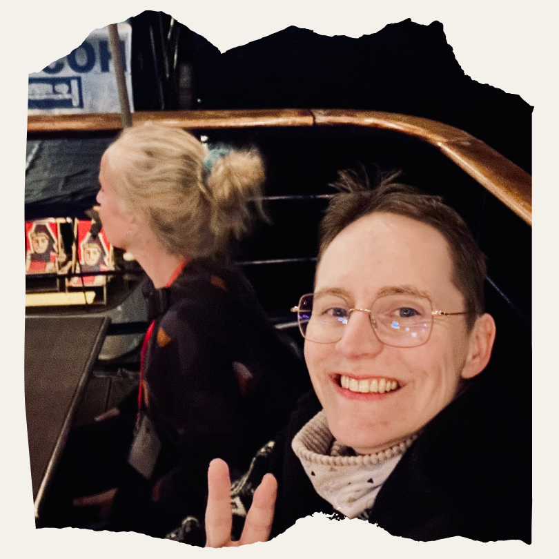Eine Person lächelt in die Kamera und zeigt das Peace-Zeichen, im Hintergrund sitzt eine weitere Person. Das Foto wurde in der Floating Lounge Berlin aufgenommen.
