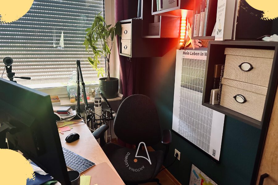 Antonia Ludwigs Homeoffice-Arbeitsplatz mit Schreibtisch, Bildschirm, Mikrofon, grüner Pflanze am Fenster, rot beleuchtetem Bücherregal mit Fachbüchern zu Psychologie und Poster 'Mein Leben in Wochen', Antonia-Ludwig-Logo eingeblendet